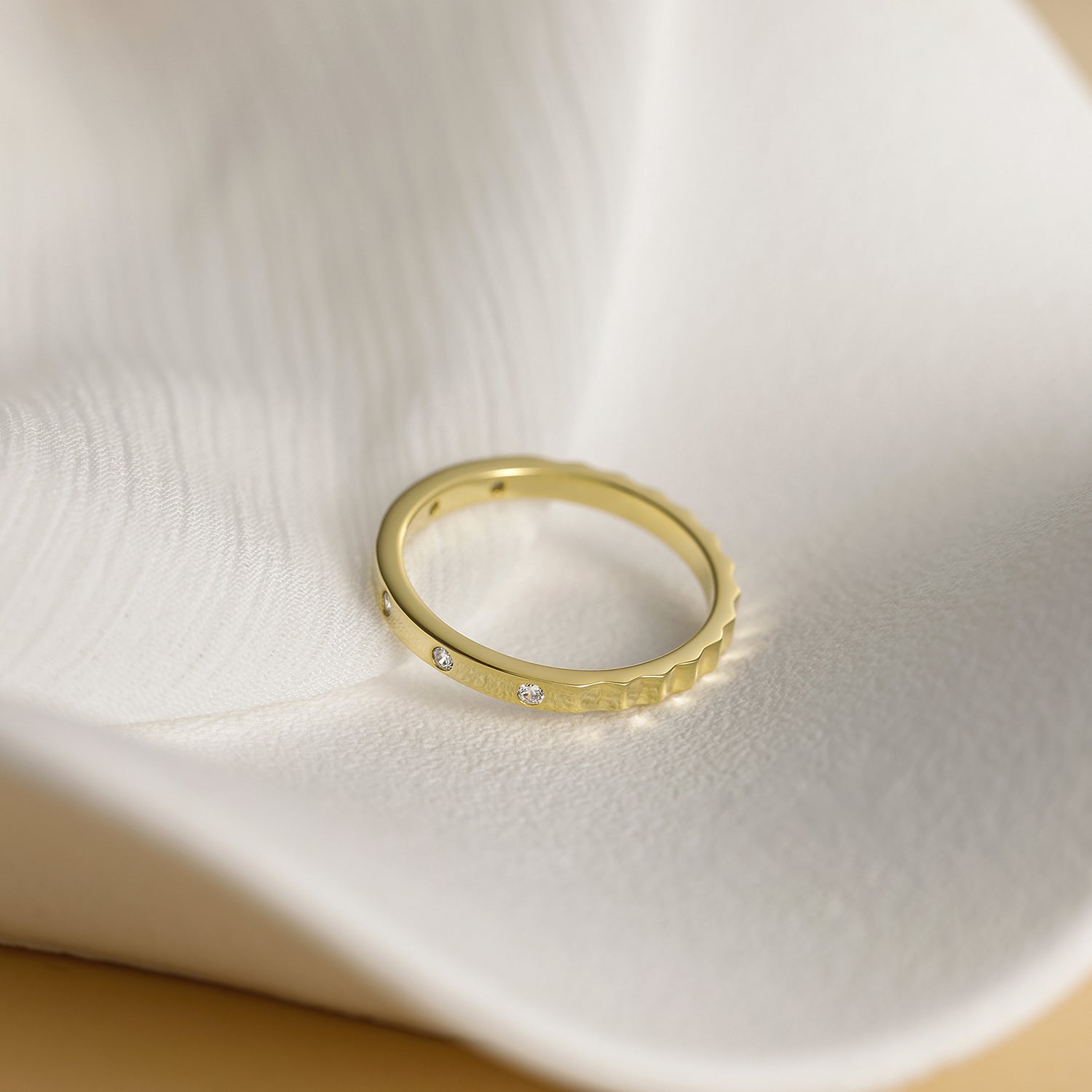 Gold ring with embedded diamonds on a textured white surface